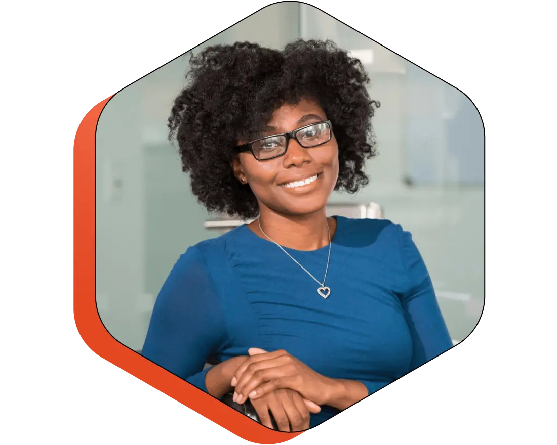Mulher negra, com cabelo solto, com blusa azul, em um ambiente aconchegante