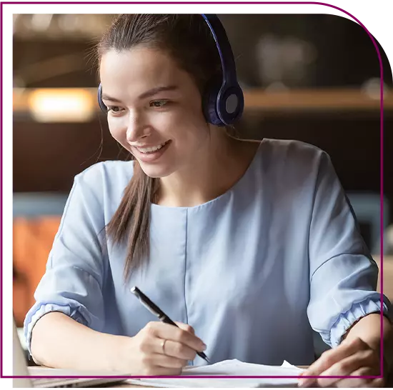 mulher branca, com cabelos castanhos e lisos, usando fones pretos, olhando para o notebook e sorrindo