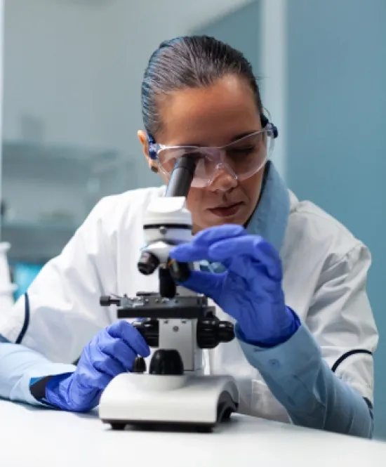 Mulher de óculos de proteção e luvas vendo um microscópio