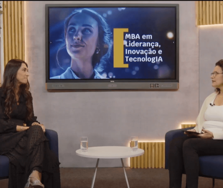 duas mulheres brancas de cabelo preto estão sentadas em duas poltronas, uma ao lado da outra. Entre elas tem uma televisão.