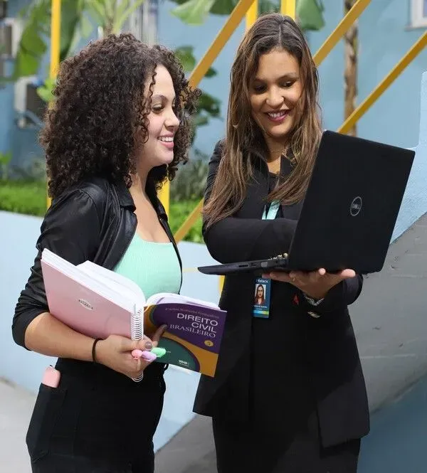 duas mulheres estudantes conversando e sorrindo com notebook e livro em mãos