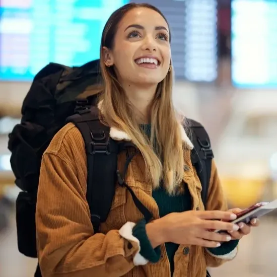 mulher branca loira sorrindo com mochila nas costas em um aeroporto