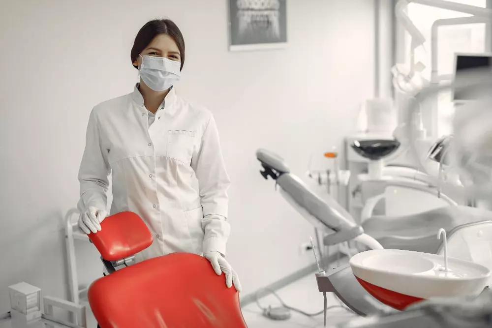 Dentista vestido de branco dentro de um consultório todo branco.