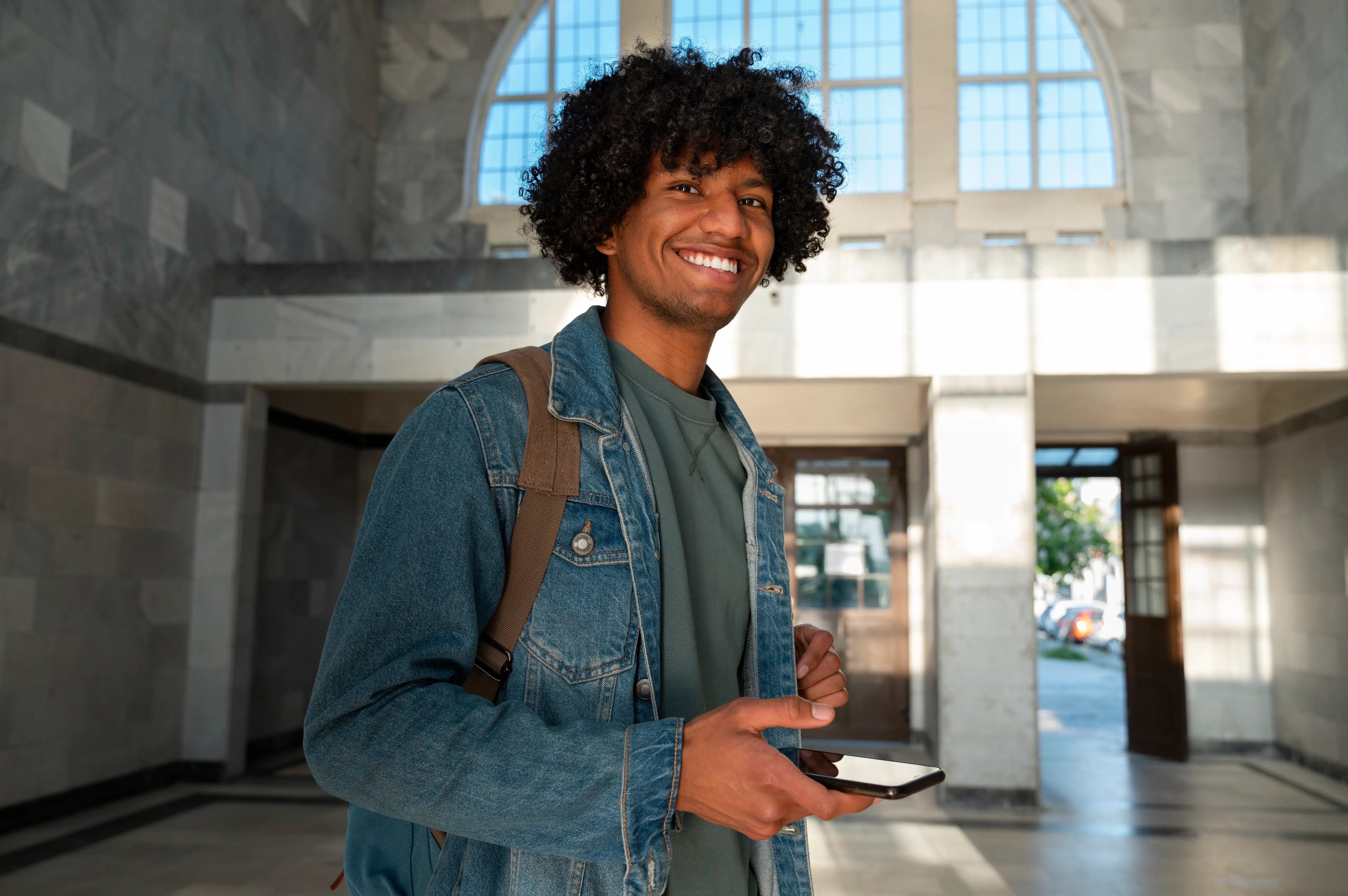 homem jovem negro sorrindo em frente a uma instituição de ensino com mochila nas costas