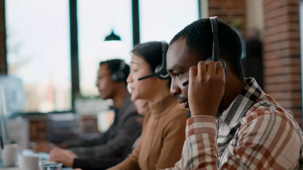 homem preto com fone de call center no ouvido, ao lado dele uma mulher branca com fone de call center no ouvido